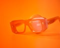An orange tub of Sarah Creal cream sitting behind orange spectacles against an orange background