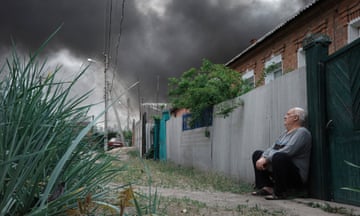 A man sits near his home in Kharkiv, Ukraine, as smoke rises above the city after Russian shelling on 17 May.