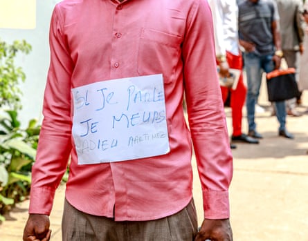 A man wears a sign which reads ‘If I speak I die, to God Martinez,’ during a ceremony to honour murdered journalist Martinez Zogo.