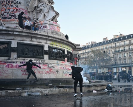 Masked protesters stand near tear gas smoke by the graffiti-covered Statue de la Republique base