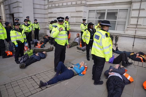 Police officers stand beside Just Stop Oil protesters lying on a pavement