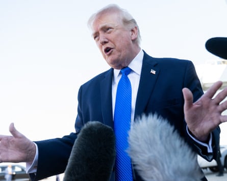 Trump wearing a blue tie speaks to reporters gesturing with his hands.