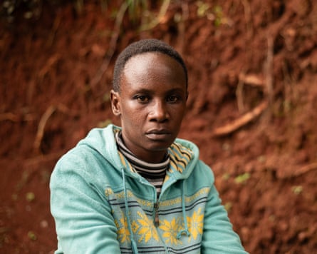 Miriam Watima sits outdoors; she has short-cropped hair and wears a pale turquoise hooded top with a yellow snowflake-like pattern across the front and a striped lining to the hood.