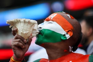 A man with orange, white and green face paint representing the Indian flag holds a shell to his mouth and blows into it in the cricket crowd