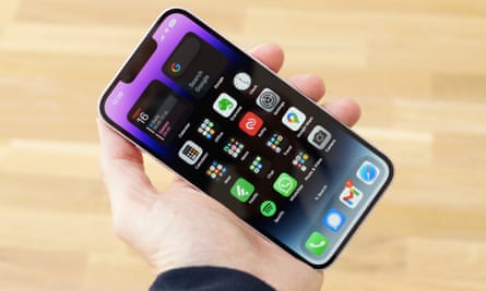 iPhone 14 is held in a hand showing the home screen.