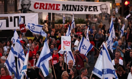 A large crowd of people at night hold Israeli flags and a large banner that says "Crime Minister".
