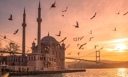 The waterside Ortaköy mosque in Istanbul, Turkey at sunrise with birds flying around it.