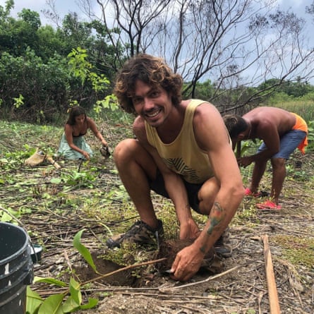 A young man smiles at the camera as he crouches to dig into soil with his bare hands.