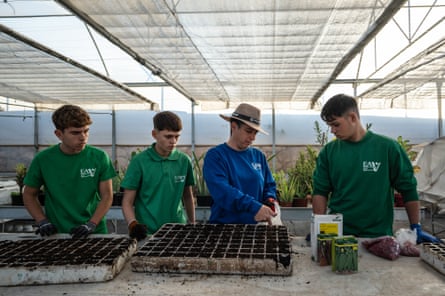 A teacher in a greenhouse pushed a finger into potted soil as the students watch