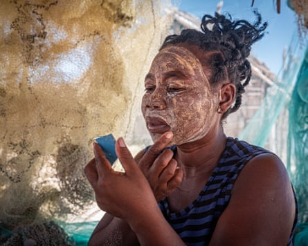 An African woman looks in a tiny mirror as she smears a yellowish paste on her face