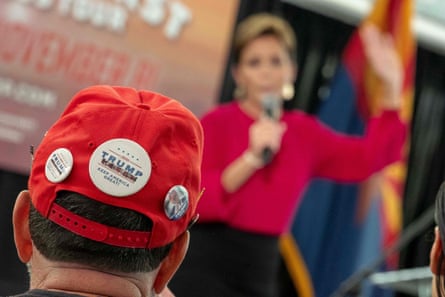 A man wearing Trump 2020 buttons on his hat listens to Kari Lake, who lost her bid for the governorship, in Phoenix.