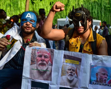 Protesters wearing superhero masks hold posters of Modi at Jantar Mantar
