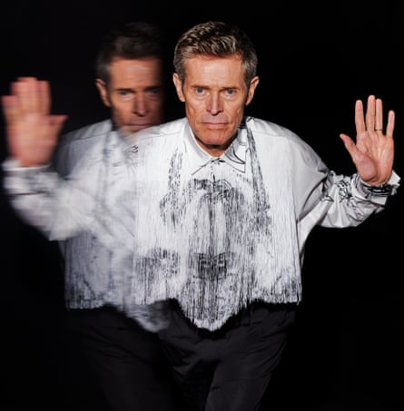 Willem Dafoe wears white shirt, with long, white and silver-grey fringe and decorative markings, and black trousers by prada.com.