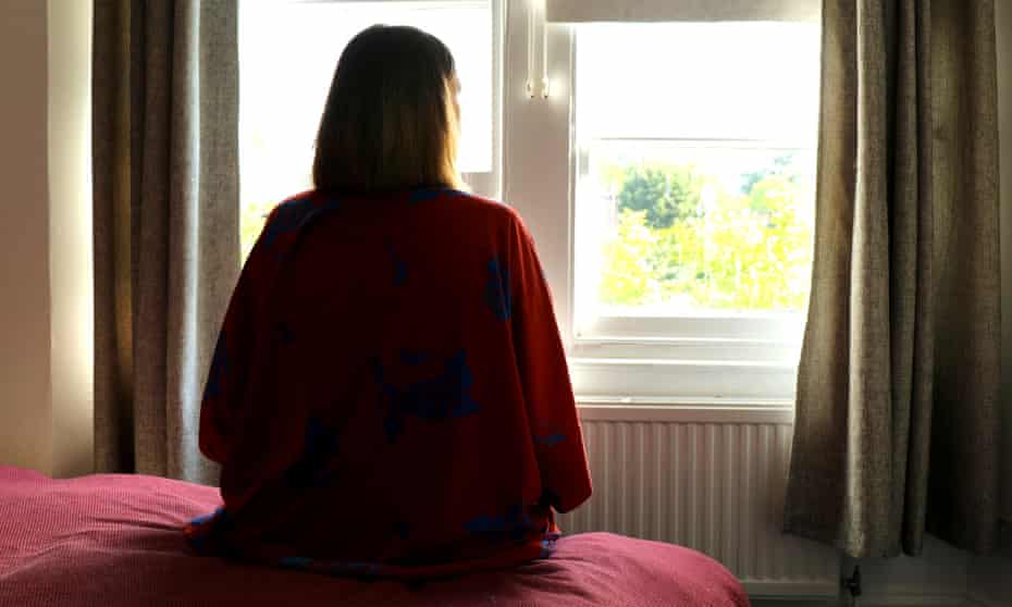 Lone woman sitting on the bed looking out of the window.