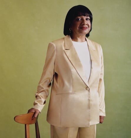 UK MP Diane Abbott in gold suit, leaning on a chair, against green background