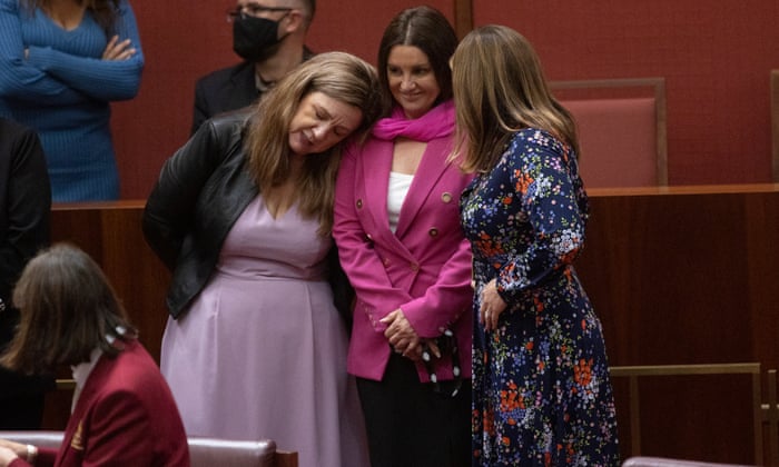 Jacqui Lambie stands in the Senate with Tammy Tyrrell standing next to her resting her head on Lambie's shoulder. Another woman whose face is obscured stands on the other side of Lambie