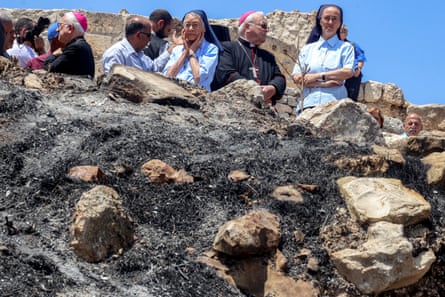 An area of burned ground, members of the Catholic clergy stand looking down at it