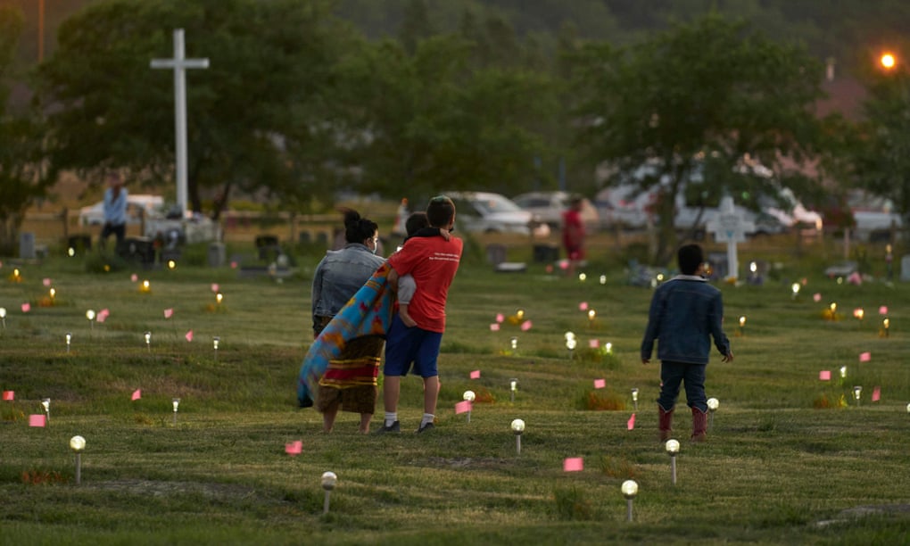 A family walks through a field where flags and solar lights now mark the site where more than 750 unmarked graves were discovered at the former Marieval Indian school in Saskatchewan on 26 June.