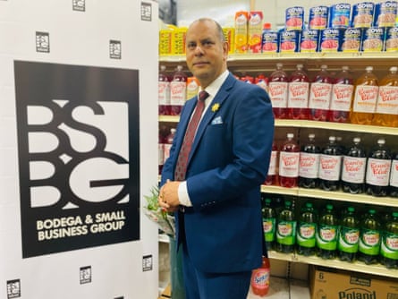 A man in a blue suit stands next to a sign reading ‘Bodega and Small Business Group’.