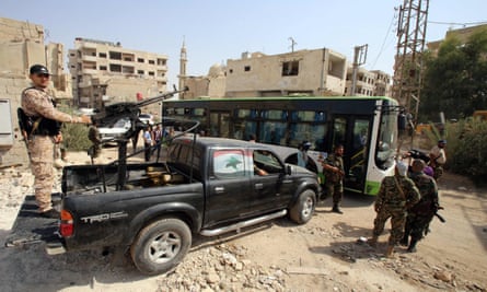 Syrian government troops stand guard as a bus carrying people drives by during the evacuation of Darayya.