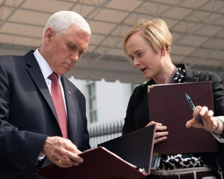 a woman holding binder speaks to a man in suit looking down at documents