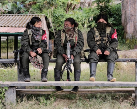 Three women in military uniforms sit on a bench in a field