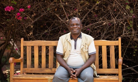 Harry Soko, who is living with cancer, sitting on a wooden bench in front of bushes, in Salima, Malawi
