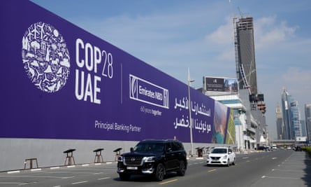 Cars pass by a billboard advertising Cop28, with skyscrapers in the background