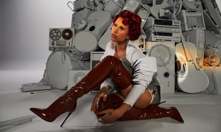 Pop star Raye sits in front of a pile of musical equipment.