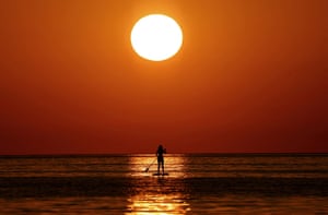 A woman paddleboards at sunrise