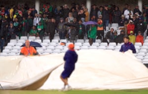 Fans look on as ground staff cover the pitch after rain stops play.