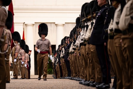 A member of the armed forces carrying a sword and wearing a bearskin hat walks past rows of military personnel