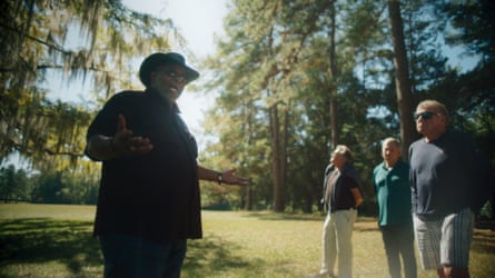 A Black man in a hat speaking to a tour group.