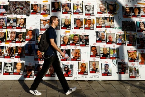 A man walks past posters on a message board with pictures of hostages