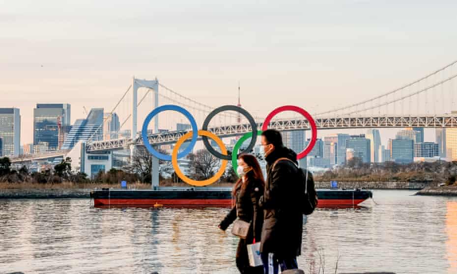 A couple wearing masks as a preventive measure against the spread of Covid-19 walks past the Olympic logo in Odaiba