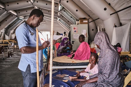 A doctor stands at the foot of a bed on whihc a young girl and a woman sit.