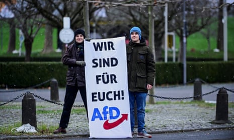 Two supporters of Alternative for Germany (AfD) holding a sign that reads ‘We are for you’ stand near German farmers taking part in a protest against the cut in vehicle tax subsidies in Bonn