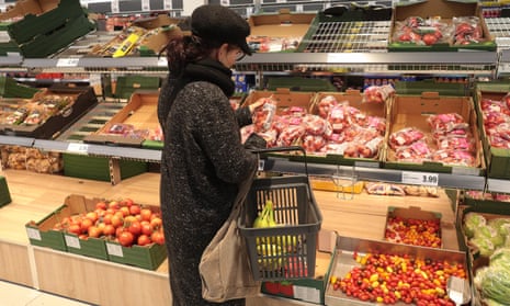 A woman looks at shelves of fruit and vegetables in a supermarket