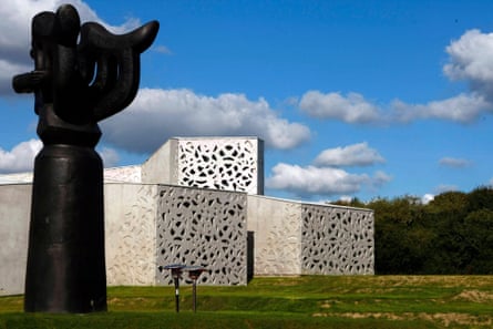 A black sculpture in front of a modern building surrounded by grass against a blue sky