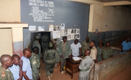 Security guards stand around a wooden desk, as people queue to be allowed through a metal door
