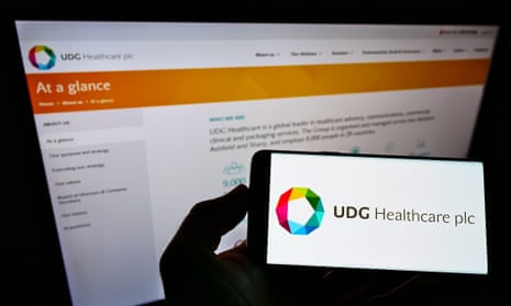 Person holding cellphone with logo of UDG Healthcare on screen in front of business webpage
