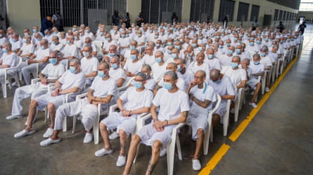 Rows and rows of inmates with shaved heads sitting on plastic chairs wearing identical clothing in a prison.