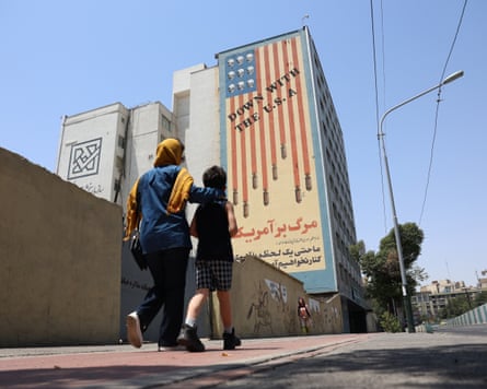 A woman and child walk past an anti-US mural on the side of high-rise building