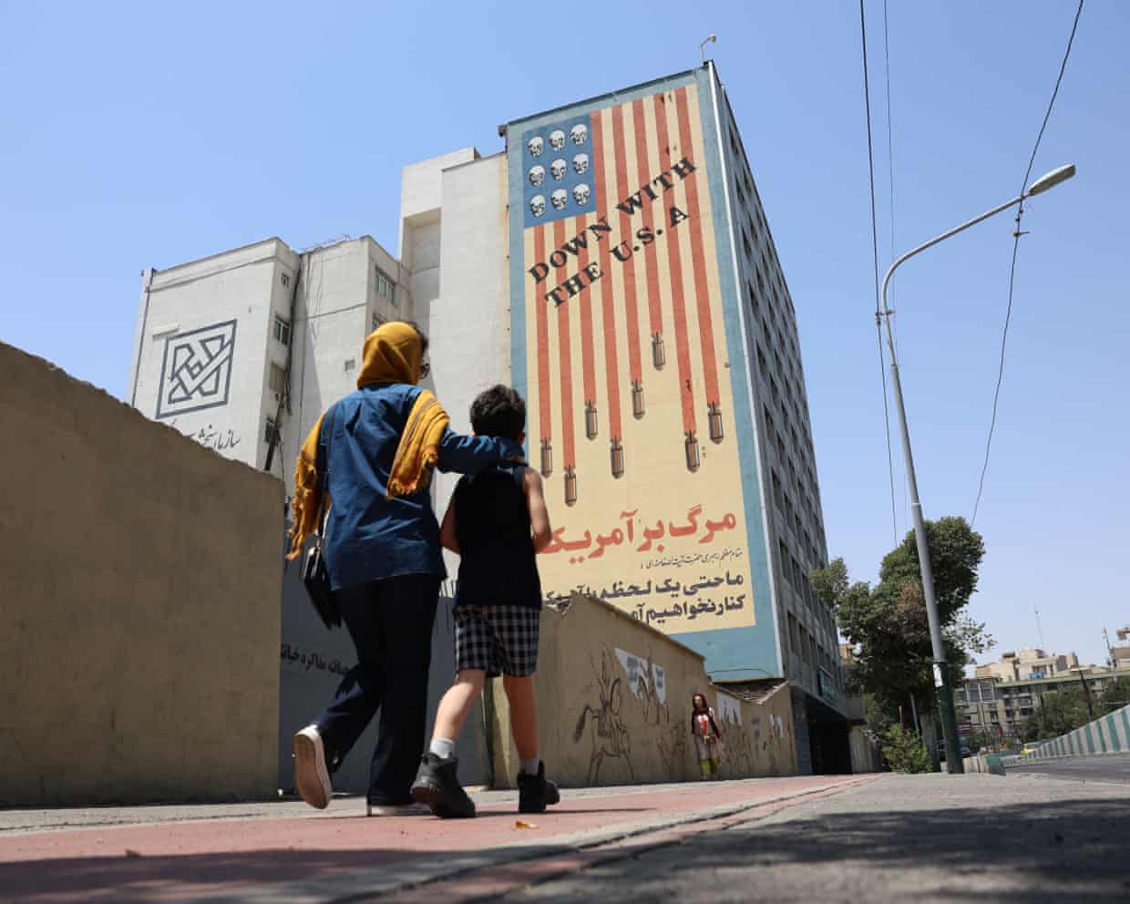 A woman and child walk past an anti-US mural on the side of high-rise building