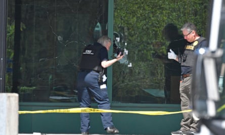 یک تکنسین پلیس مترو لوئیزویل از سوراخ های گلوله در شیشه جلوی ساختمان بانک ملی قدیمی عکس می گیرد.