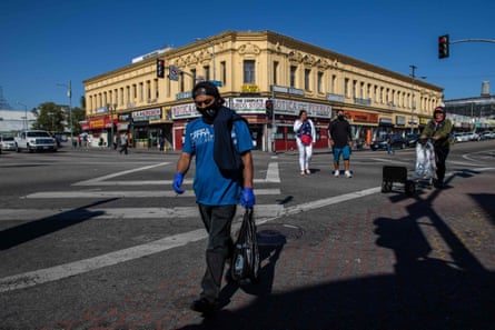 A Latino worker wears a mask and gloves as he crosses a street in the MacArthur Park area of Los Angeles.