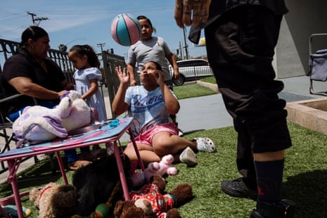 Kids play at a table in a yard with a ball and stuffed animals