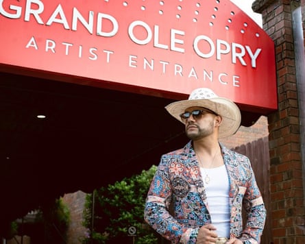 A man in a cowboy hat and paisley blazer stands outside the artist entrance of the Grand Ole Opry