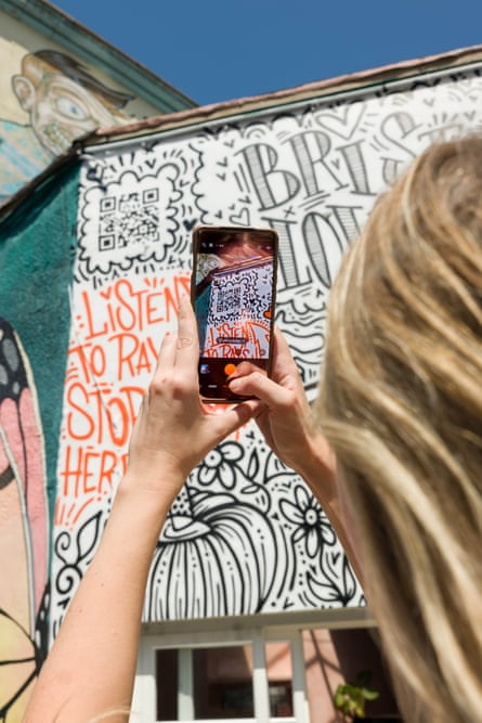 A woman using a smartphone to scan a QR code on the mural in Bristol