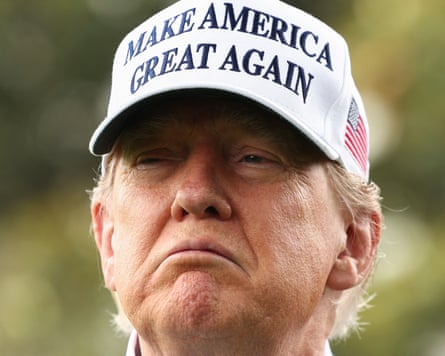 Close up of a frowning Donald Trump wearing a white 'Make America Great Again' cap